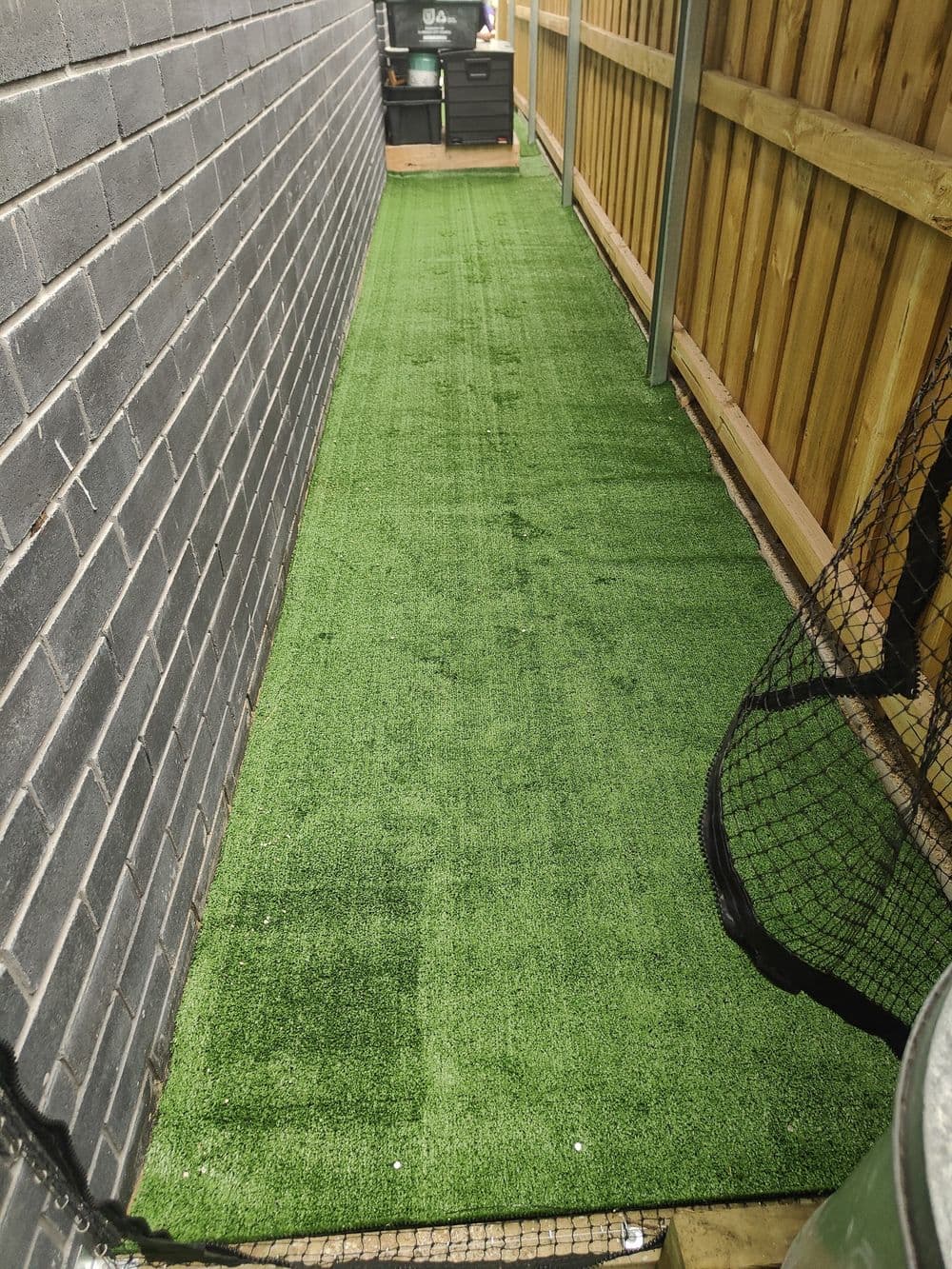 A long netted cat run with artificial turf between a house and a timber fence
