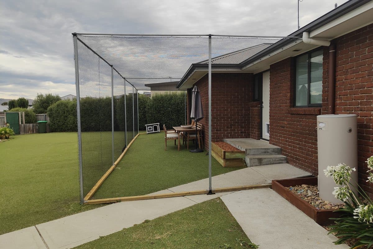 A netted enclosure covering a whole backyard lawn behind a brick home