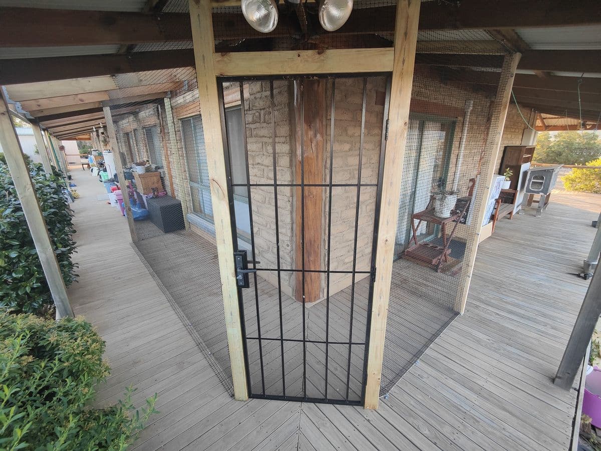 A black barred gate set into a timber frame across an enclosed verandah, with the verandah continuing beyond