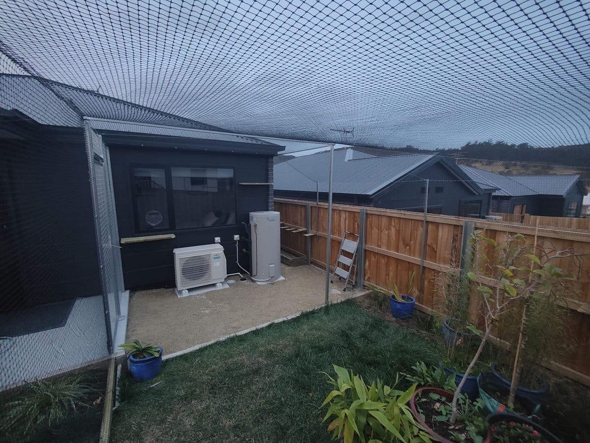 Netting stretched over a small back yard with lawn and pot plants beside a dark clad house and a timber fence