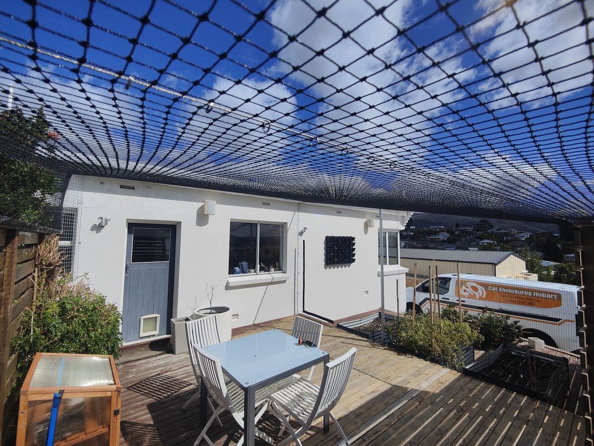Black netting over a timber deck with a white outdoor setting and timber slat screens beside a white house