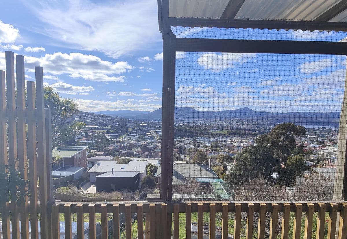 A covered balcony enclosed with netting above timber railings, looking out over the city to the mountains