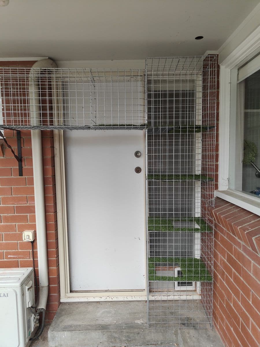 A compact galvanised mesh catio built around a back door, with turf-covered shelves stacked up the side